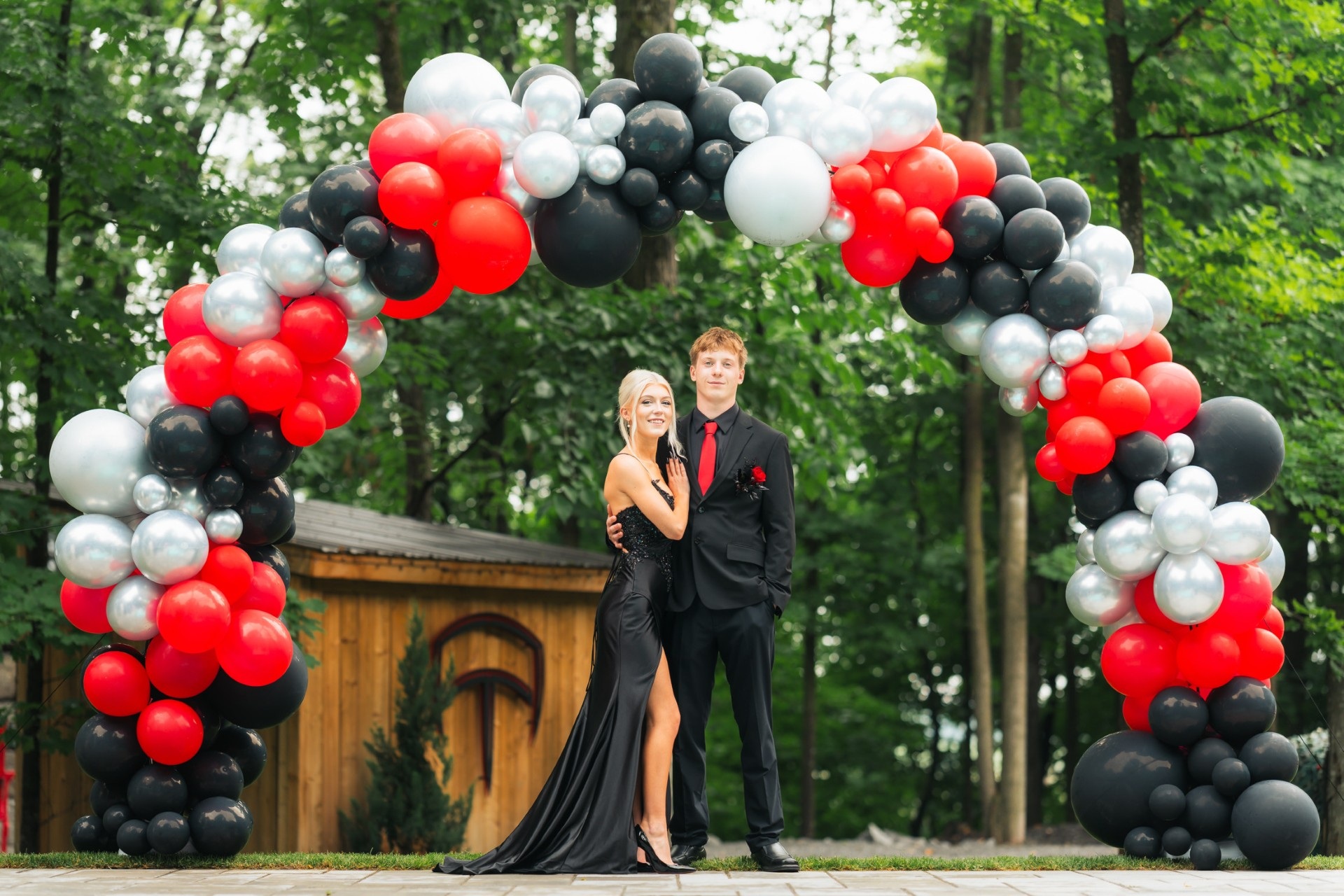 Red, black and silver graduation balloon arch outdoors with two graduates standing beneath it